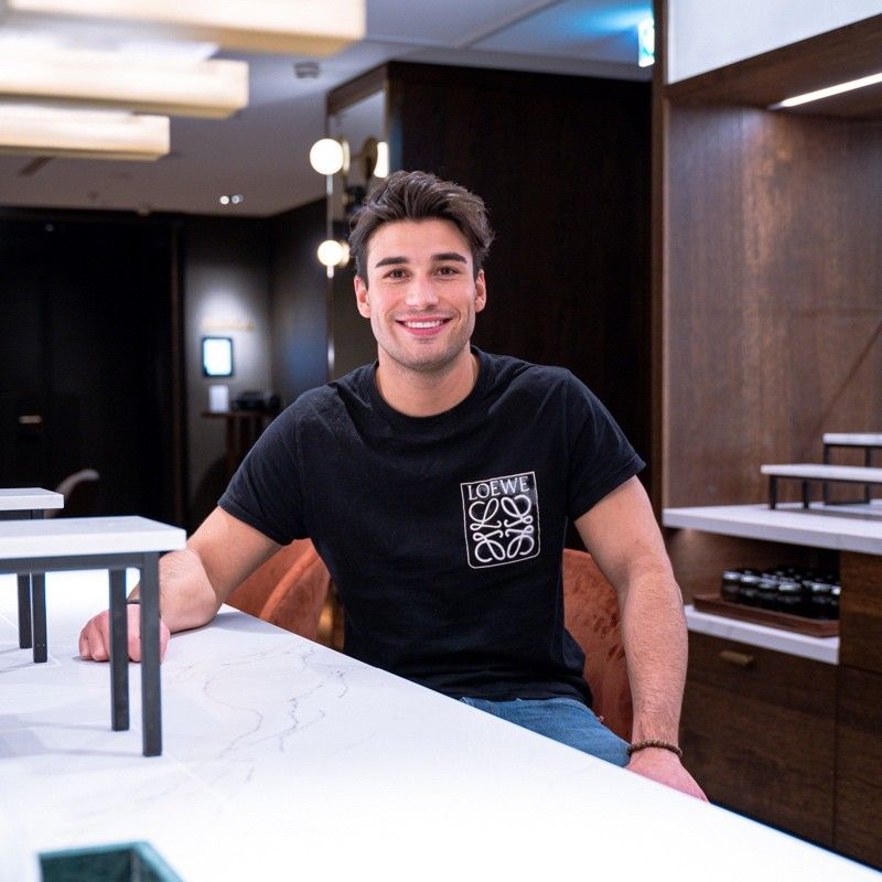 A man wearing a loewe shirt sits at a counter