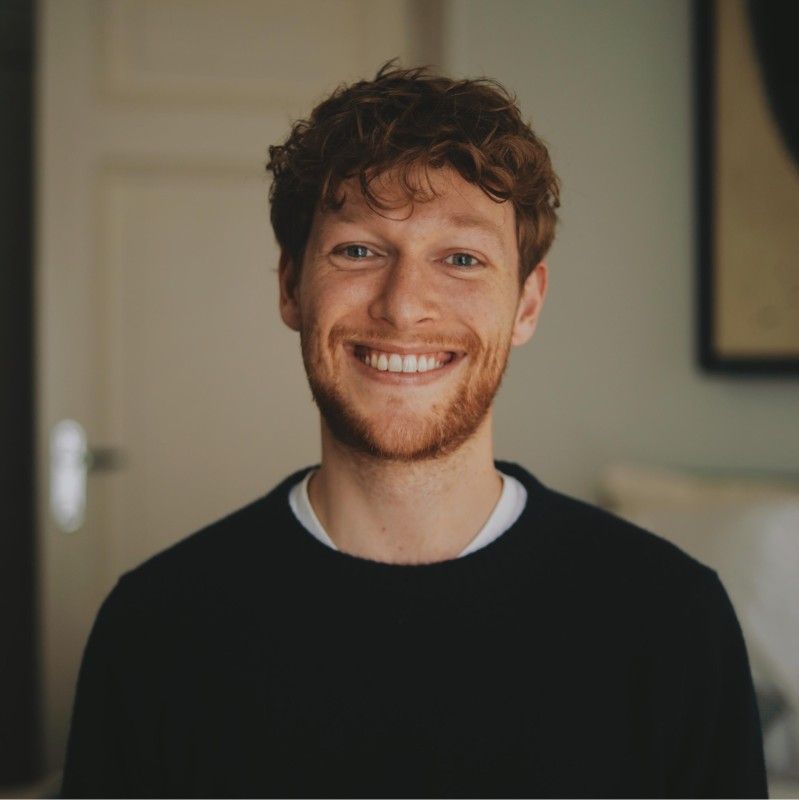 A man with a beard is smiling for the camera while wearing a black sweater.