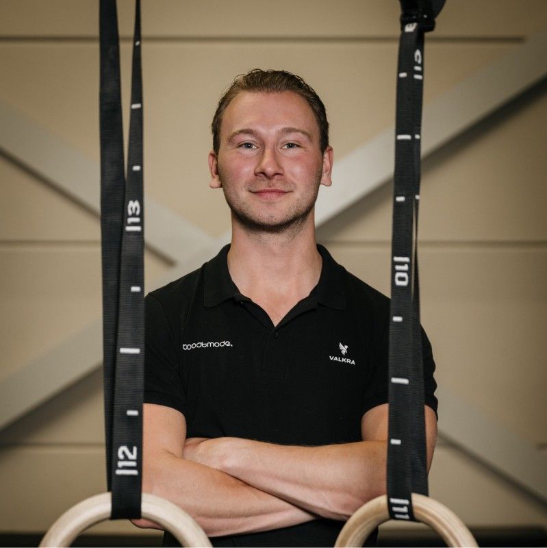 A man in a black shirt is standing in front of gymnastic rings