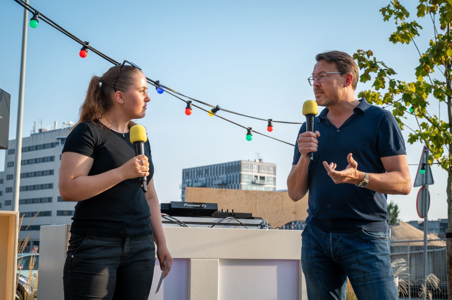 A man and a woman are standing next to each other talking into microphones.