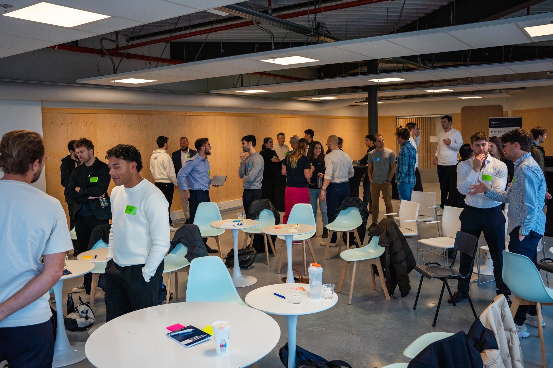 A group of people are standing around tables and chairs in a room.