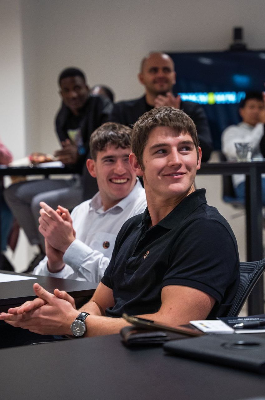 A group of young men are sitting at a table applauding.