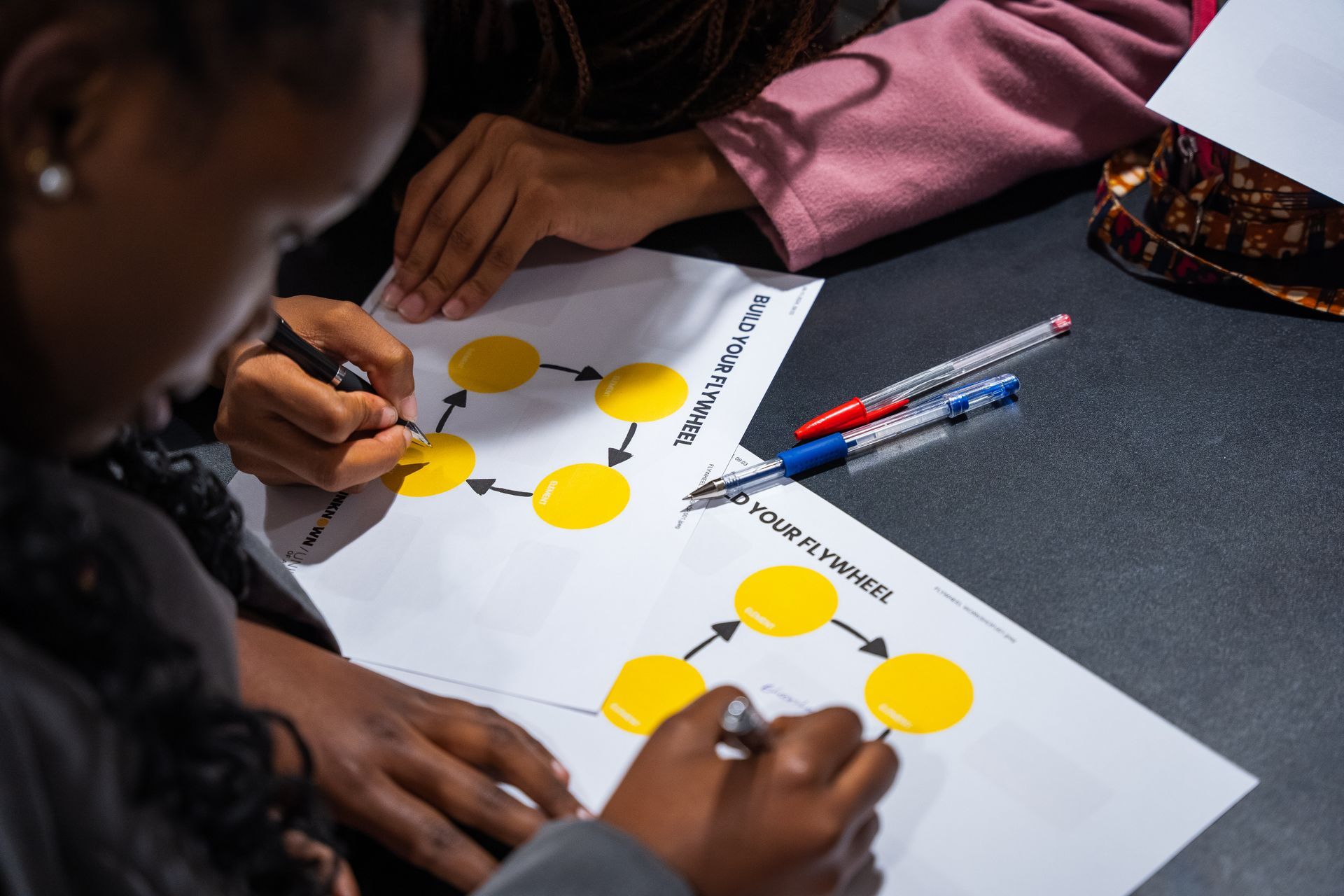 A group of children are sitting at a table writing on a piece of paper.
