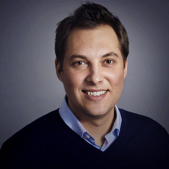 A man wearing a blue sweater is smiling for the camera