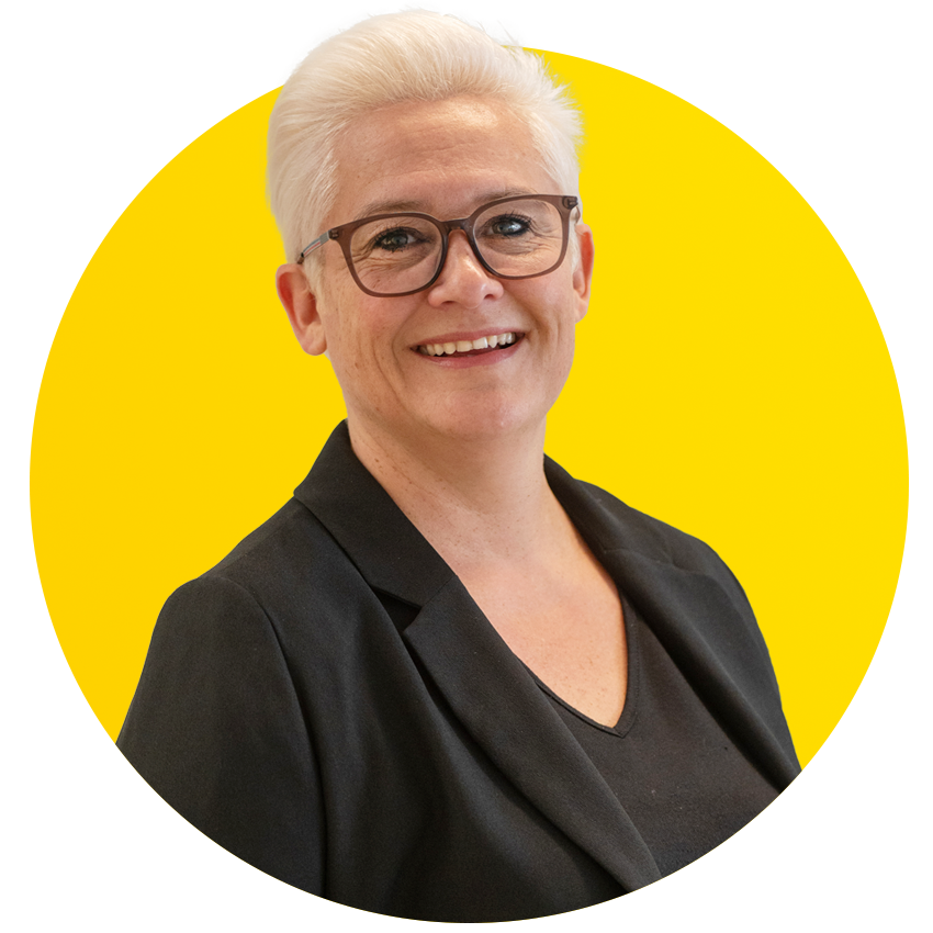 A woman wearing glasses and a black jacket is smiling in a yellow circle.
