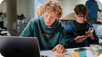 A group of people are sitting on benches in front of a large building.