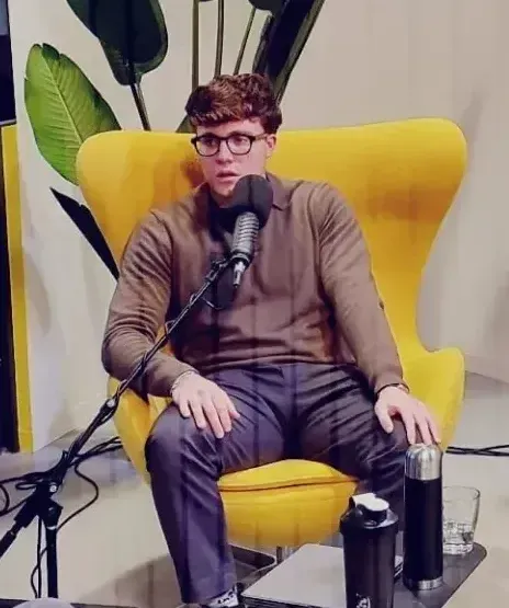 A man wearing glasses is sitting in a yellow chair with a microphone
