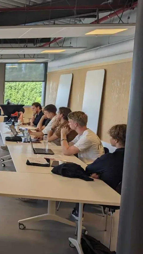 A group of people are sitting at long tables in a conference room.