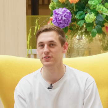 A young man is sitting in a yellow chair with flowers in the background