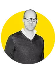 A man wearing glasses and a black sweater is standing in a yellow circle.