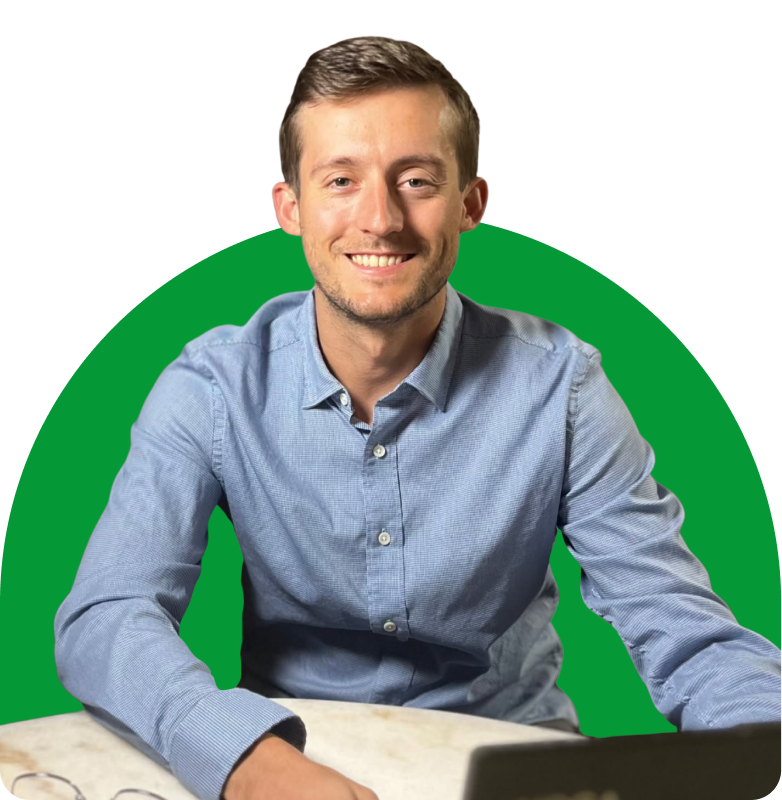Smiling man in a blue shirt sitting at a desk against a green circular background