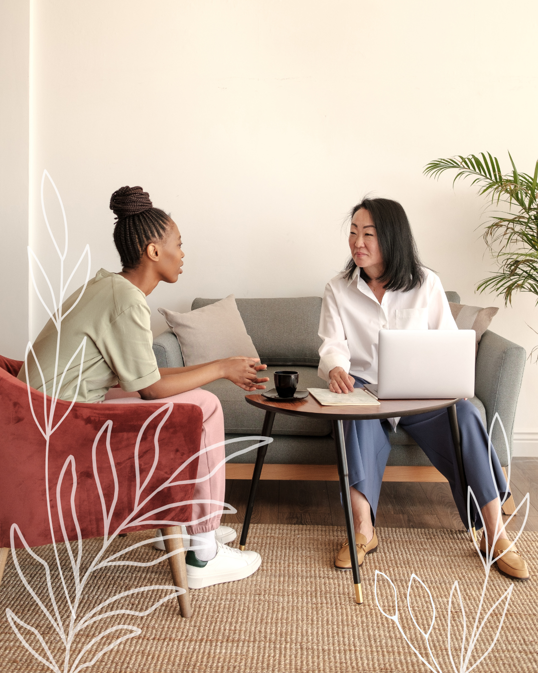 Two people sit in a cozy room, one on a velvet chair and one on a sofa, engaged in a conversation across a small table.