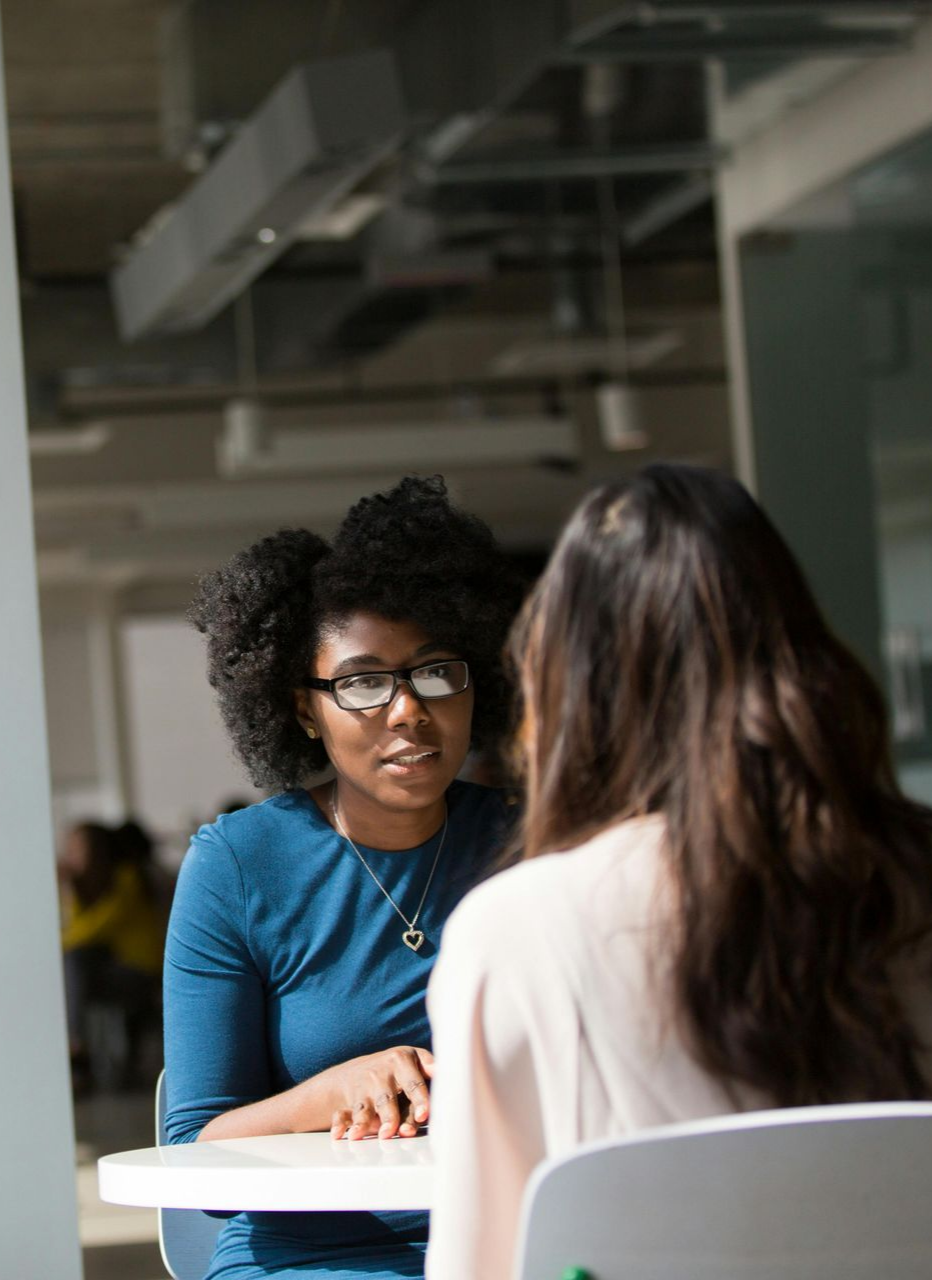 Two people sit at a white table in a bright, modern office, engaged in a focused conversation.