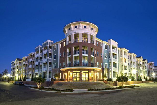 Apartment building at dusk; beige, teal, and brick exterior, lit entryway, multi-story structure at Town Center at Lake Carolina in Columbia, SC.