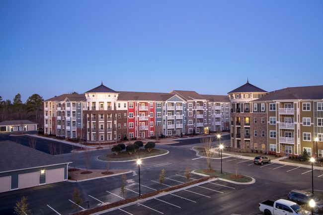 Apartment complex with colorful exterior, circular drive, and parking lot at dusk at Town Center at Lake Carolina in Columbia, SC.