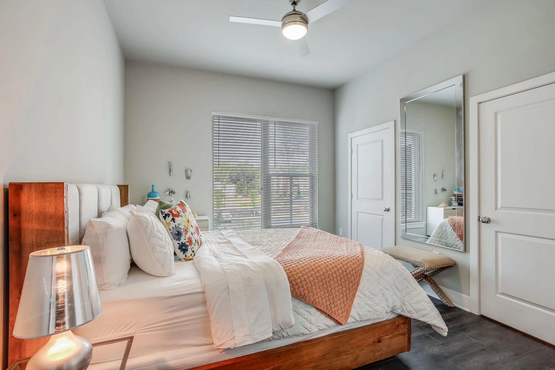 A bedroom with a large bed , a ceiling fan , a mirror and a sliding glass door.
