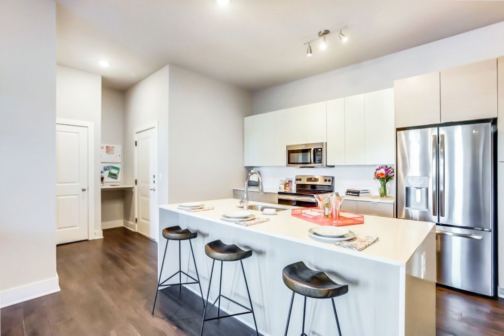 A kitchen with a large island , stools , a refrigerator and a microwave.