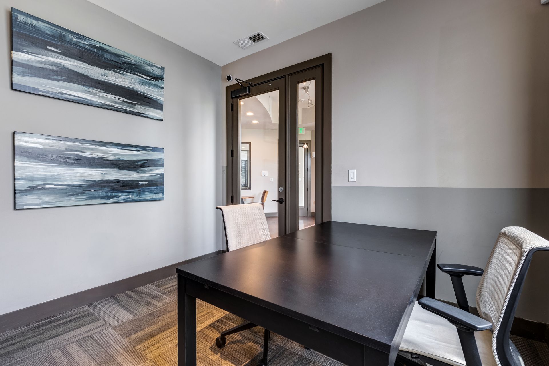 Office space with a black desk, two chairs, abstract art, and a doorway at Town Center at Lake Carolina in Columbia, SC.
