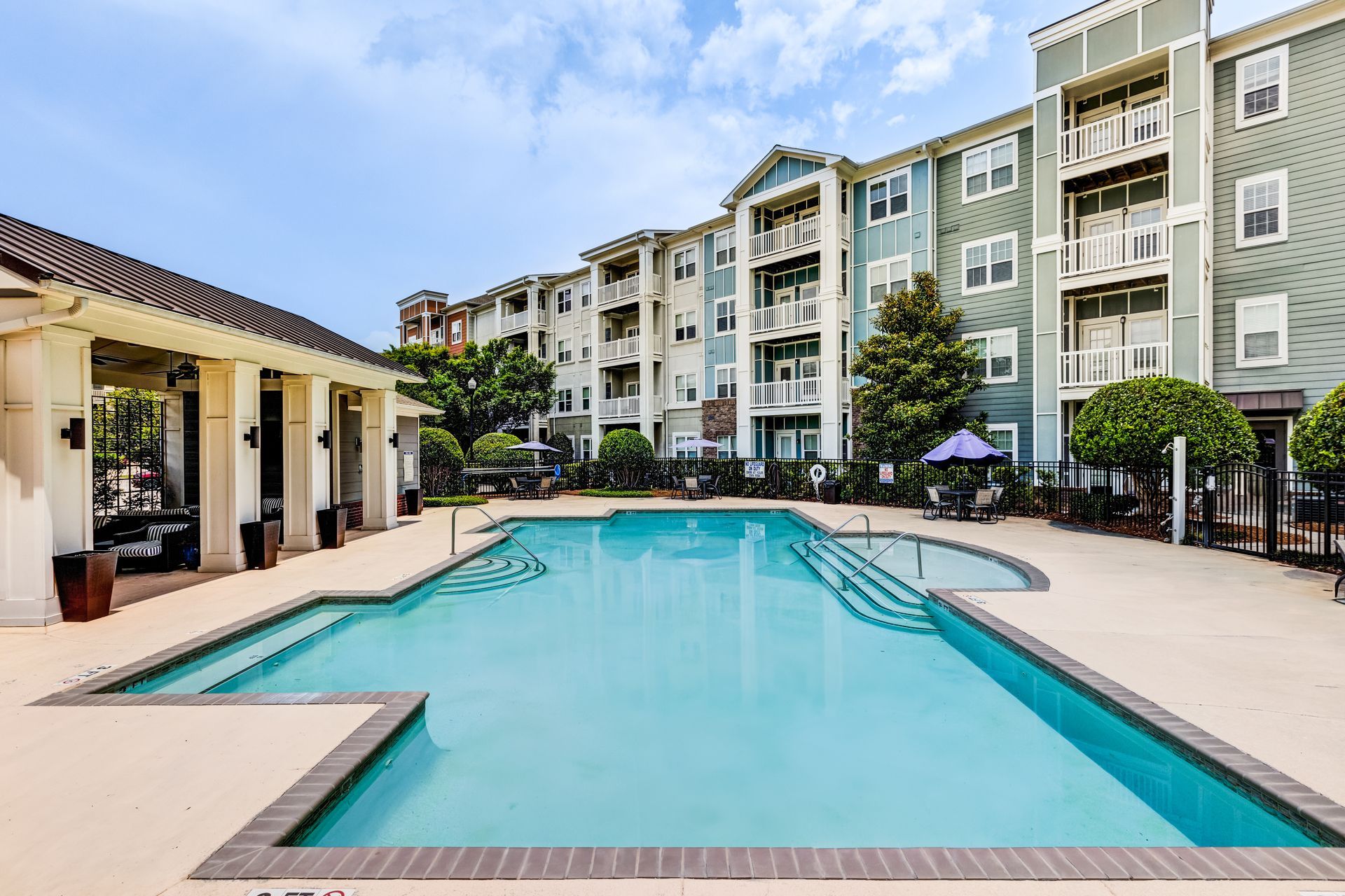 Pool with clear blue water in front of a multi-story apartment building under a blue sky at Town Center at Lake Carolina in Columbia, SC.