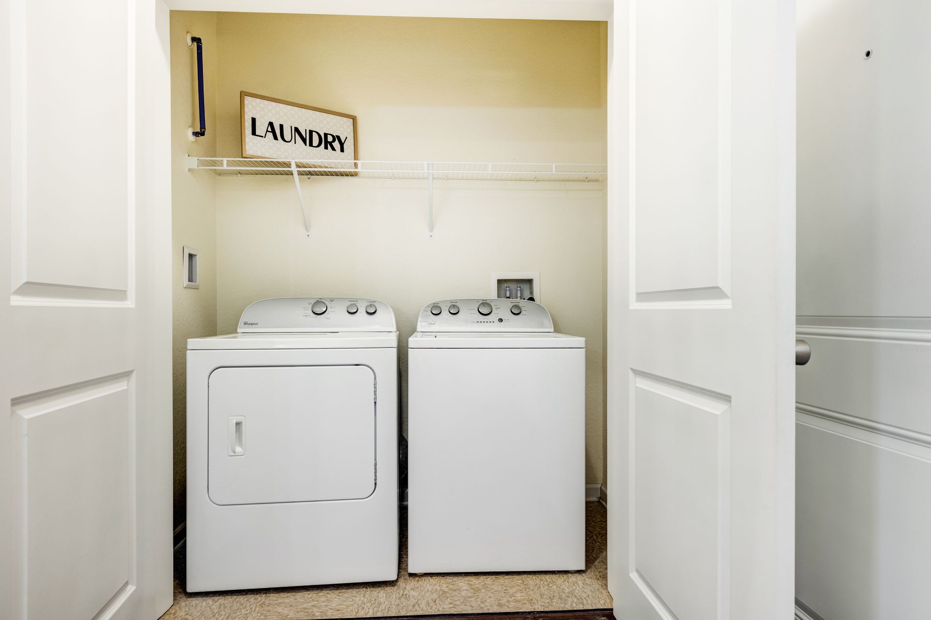 Laundry room with white washer and dryer, laundry sign, and white shelves at Town Center at Lake Carolina in Columbia, SC.