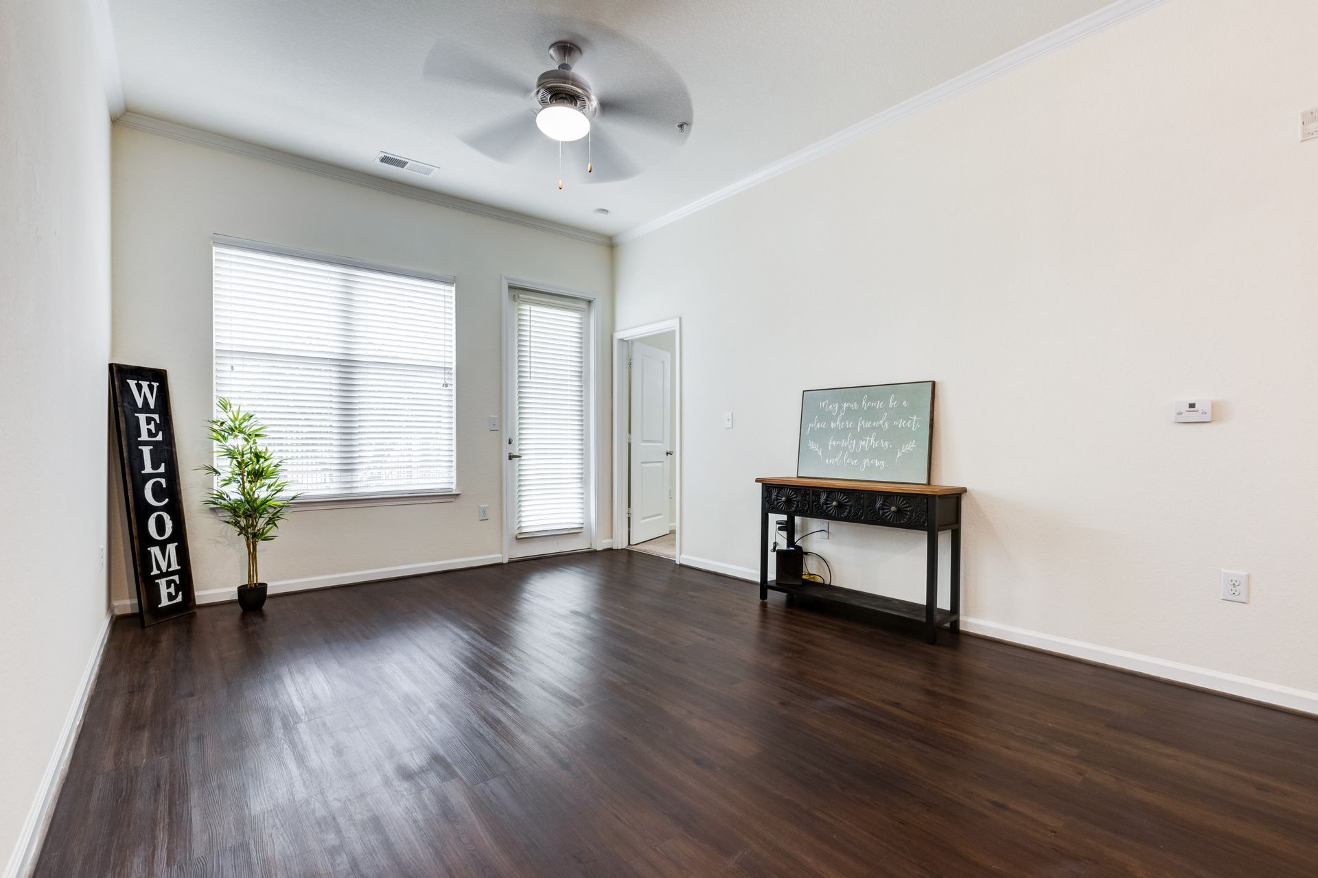 Empty living room with dark wood floors, large window, and a welcome sign at Town Center at Lake Carolina in Columbia, SC.