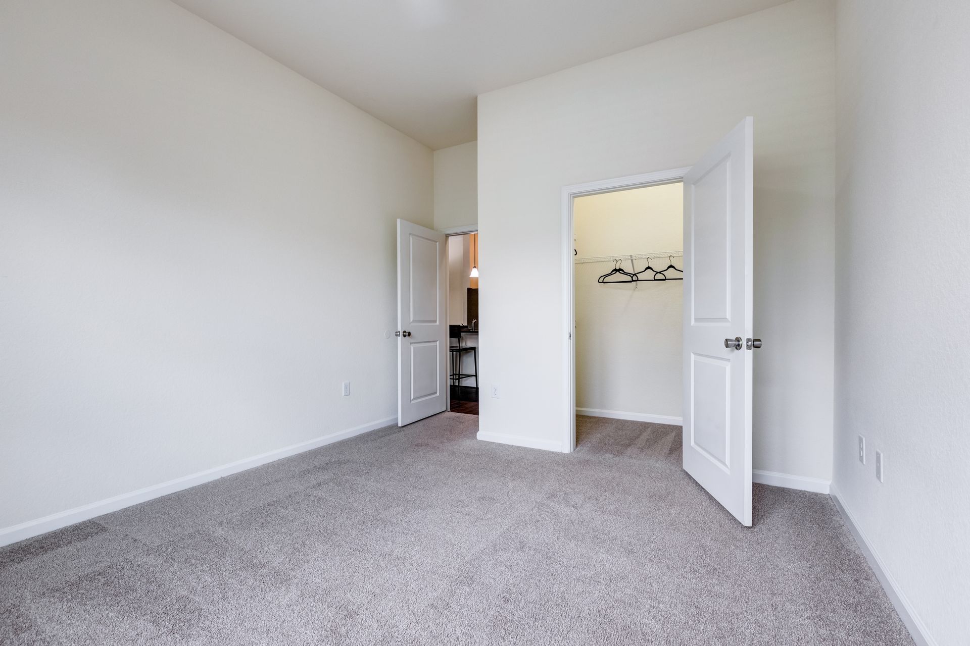 Empty bedroom with neutral walls, gray carpet, and two white doors, one open to a closet at Town Center at Lake Carolina in Columbia, SC.