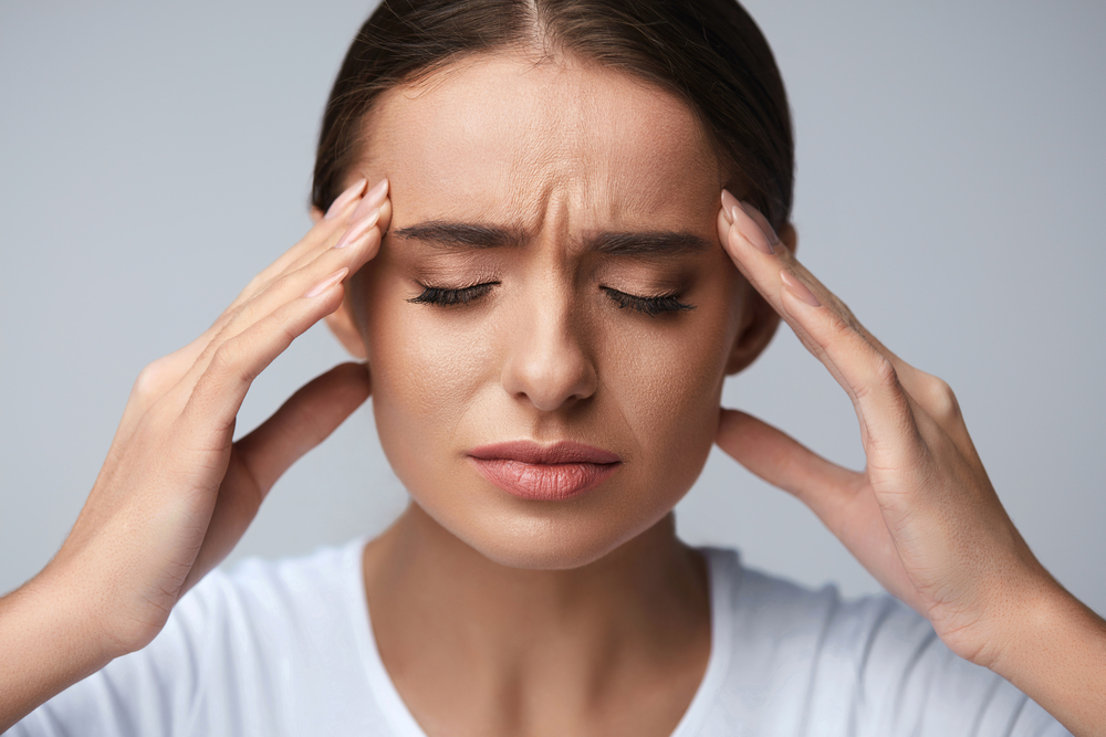 Woman with hands on temples, eyes closed, showing pain.