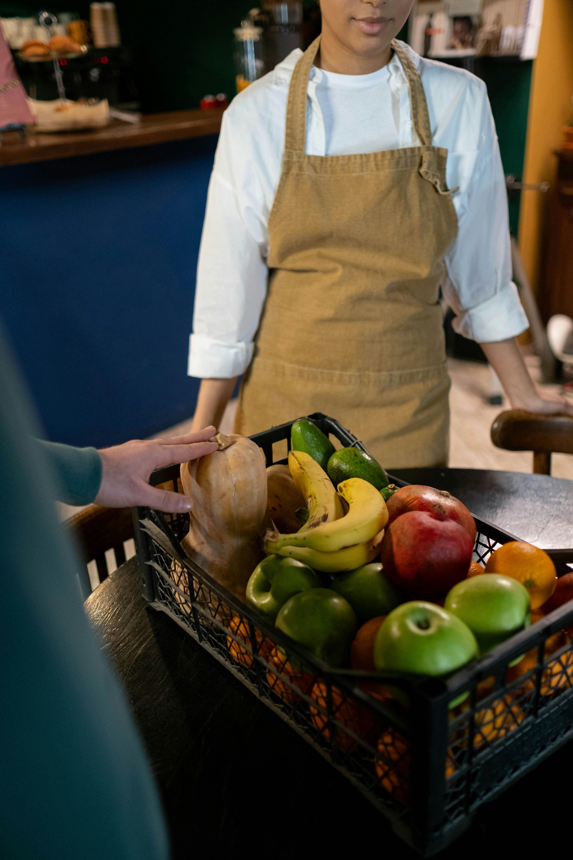 A person hands an item to a server standing behind a fruit basket at a cafe.