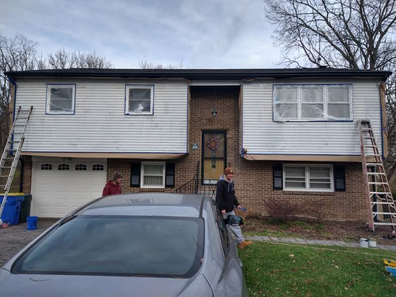 A man is standing in front of a house with a car parked in front of it.