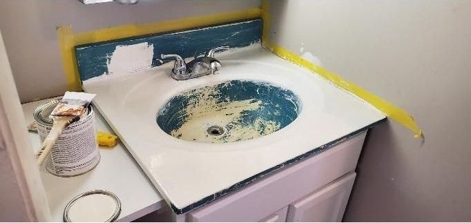 A bathroom sink is being painted with a can of paint and a brush.