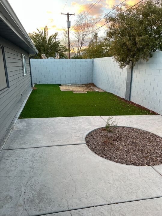 A backyard with a concrete walkway and a lush green lawn.