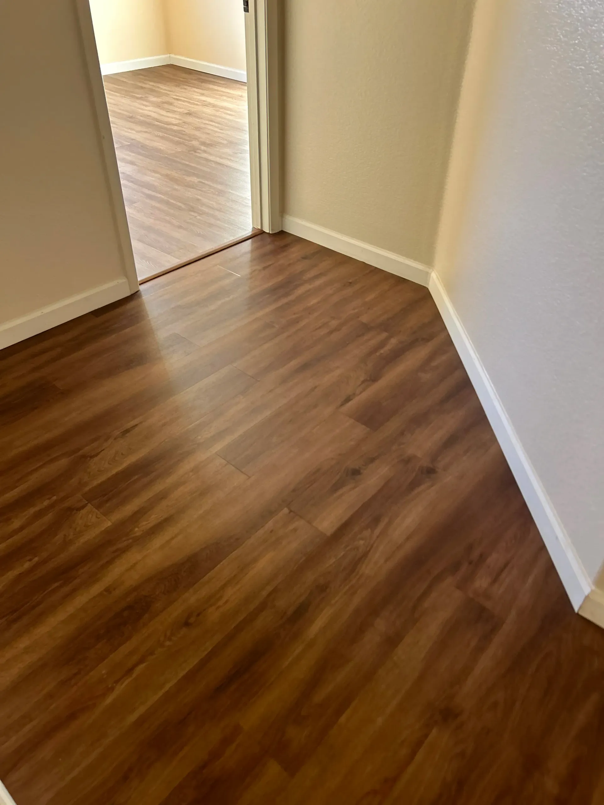 A hallway with hardwood floors and a door leading to a room.
