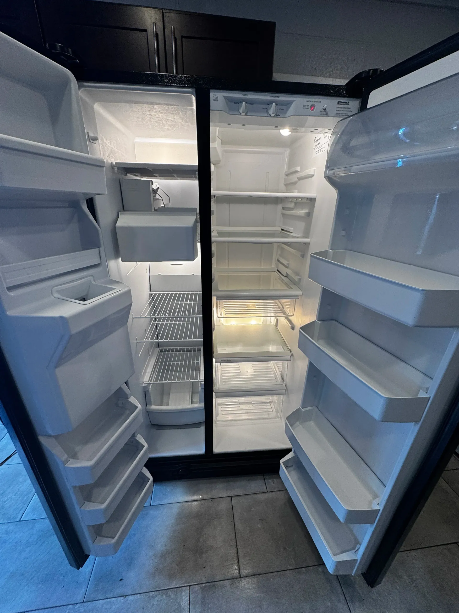 An empty refrigerator with its doors open in a kitchen.