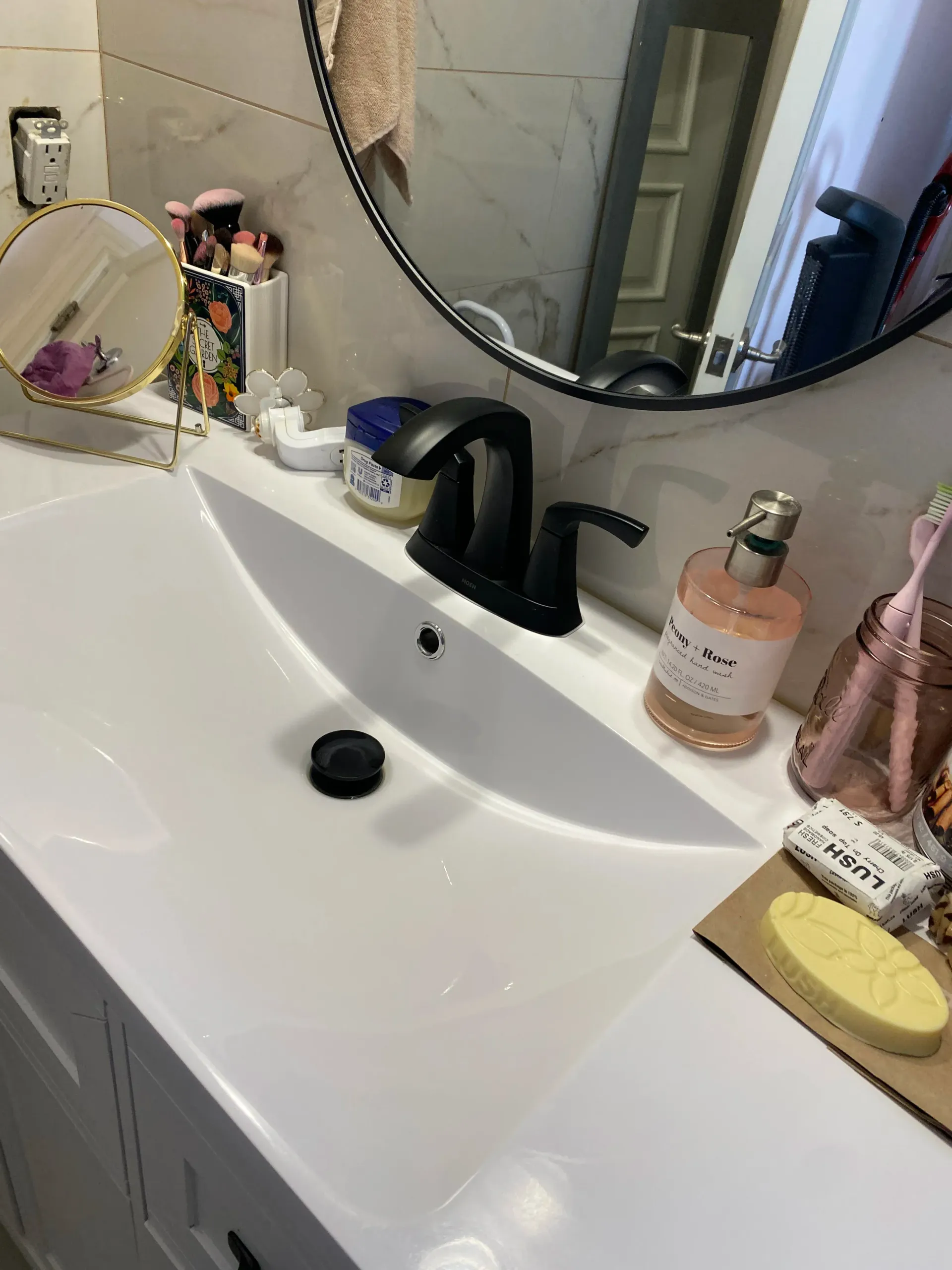 A bathroom sink with a round mirror and a soap dispenser.