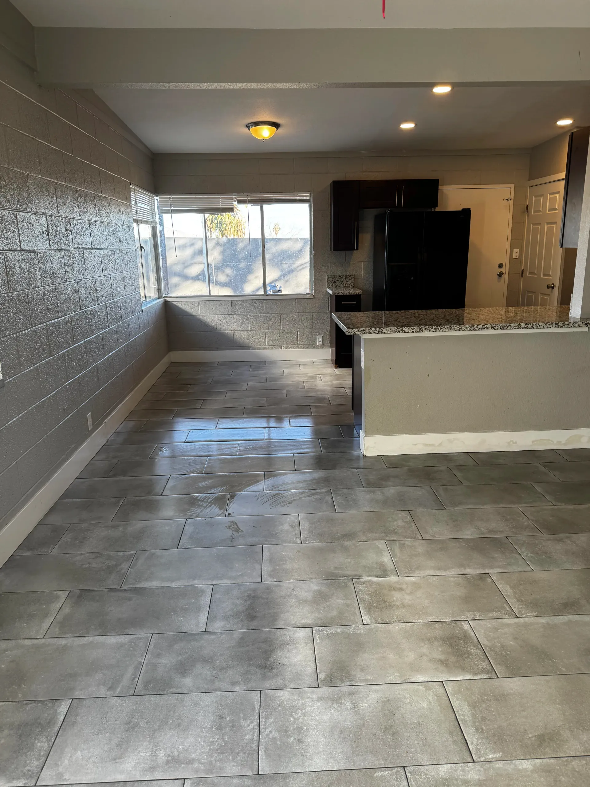 A living room with a tiled floor and a kitchen in the background.