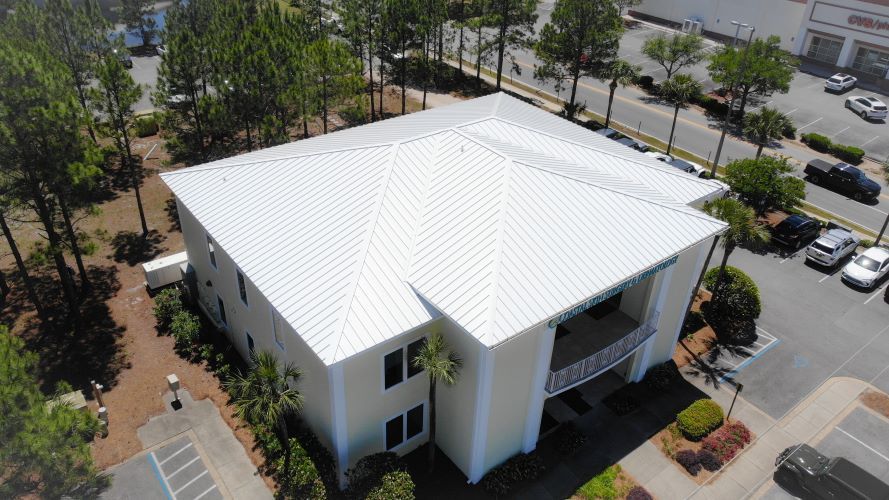 An aerial view of a large white building with a white roof surrounded by trees.