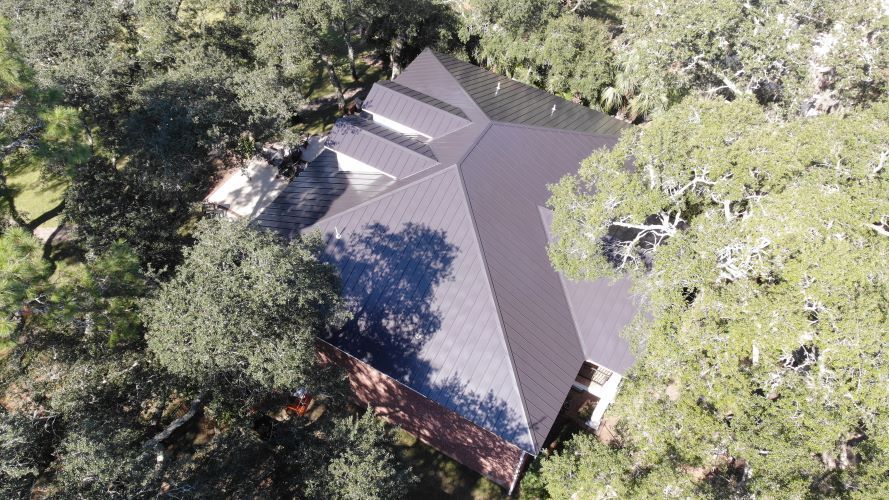 An aerial view of a house with a black roof surrounded by trees.