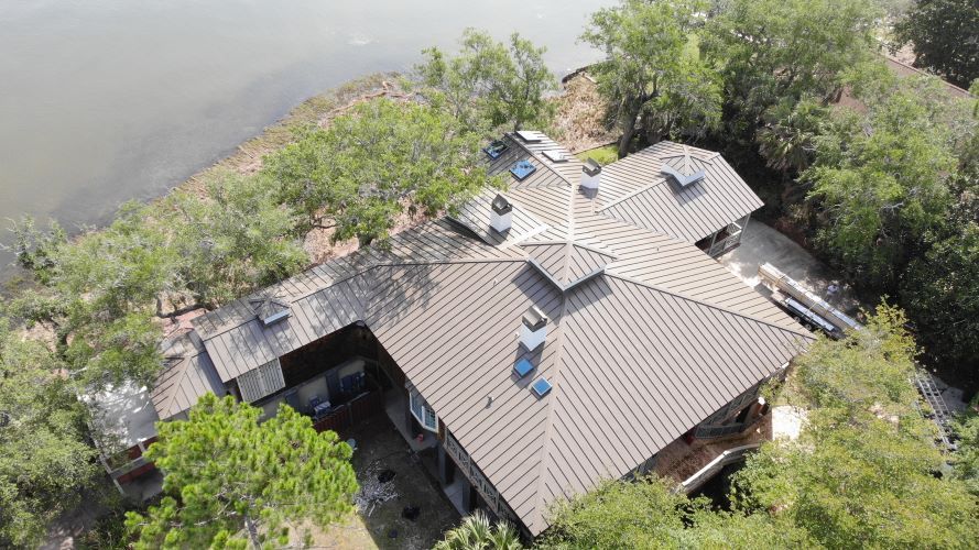 An aerial view of a house next to a body of water surrounded by trees.