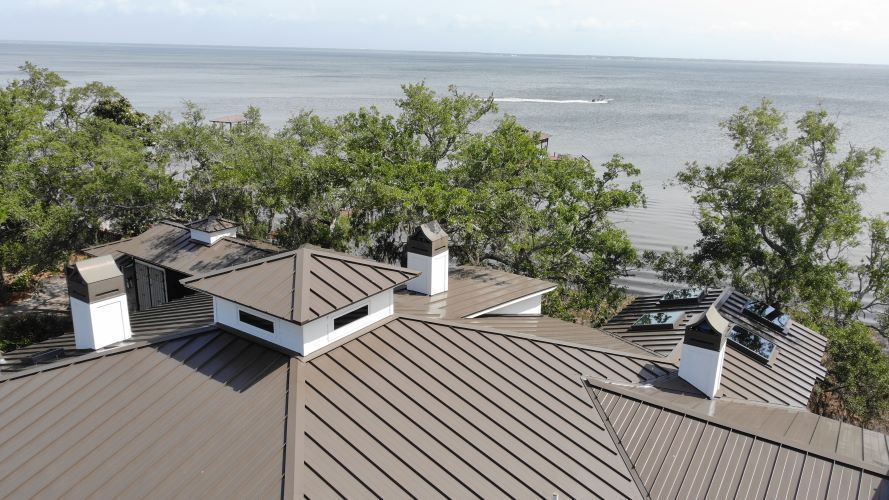 An aerial view of a house with a metal roof overlooking the ocean.