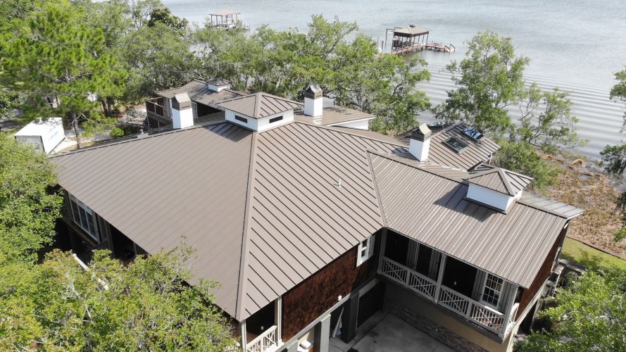 An aerial view of a house with a metal roof next to a body of water.