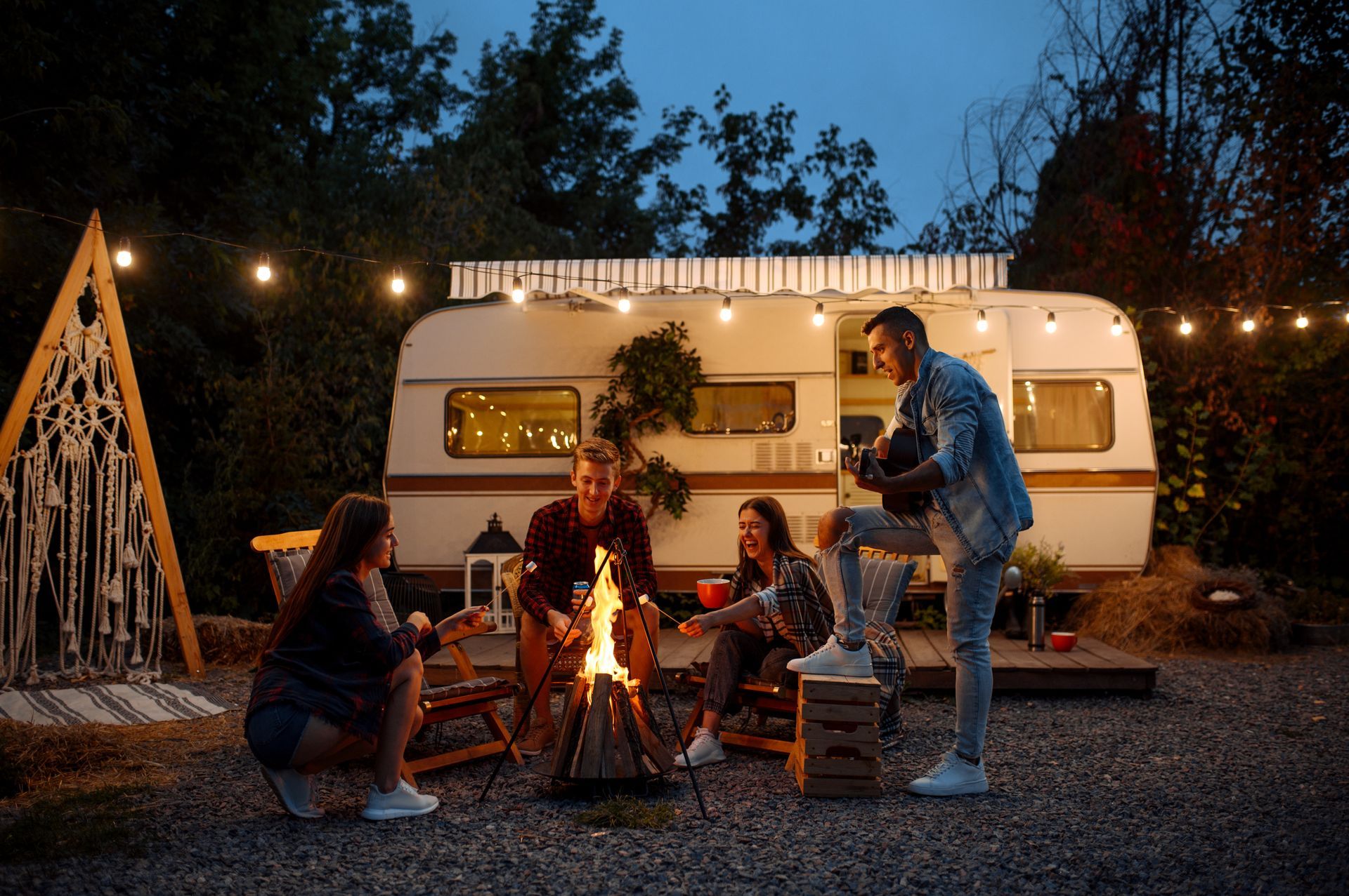 A group of people are sitting around a campfire in front of a trailer.