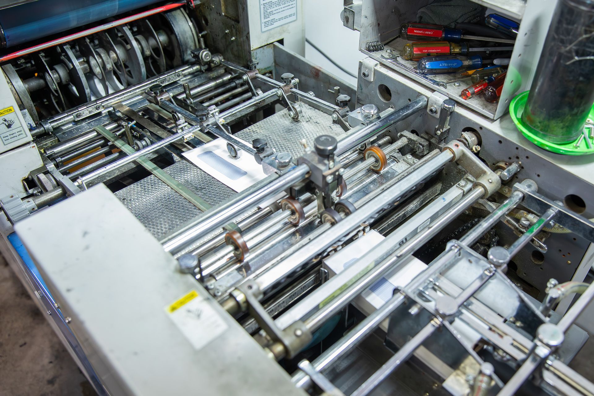 Folding machine with paper sheets inside, showing gears and rollers.