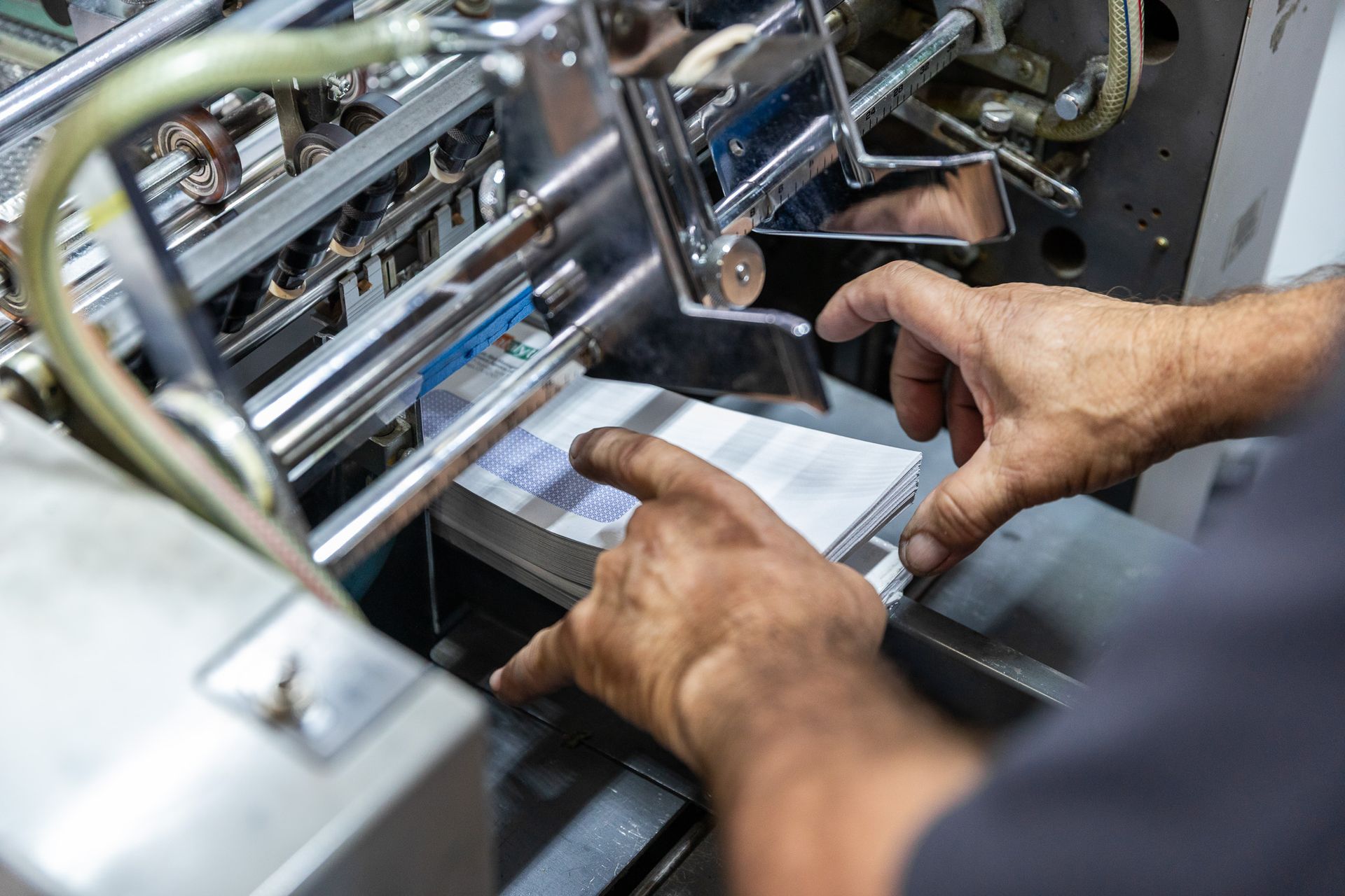 Hands of a person aligning a stack of printed pages in an industrial printing machine.
