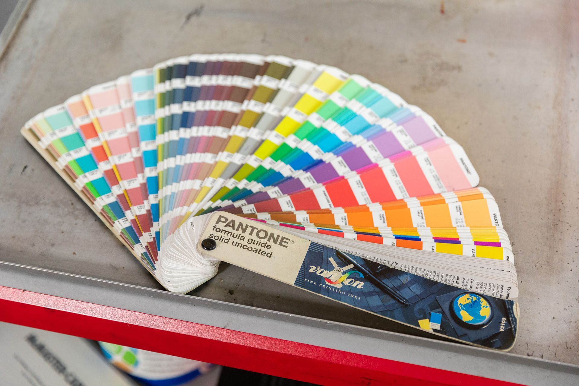 Pantone color swatch fan, open, displaying numerous color samples on a metal surface.
