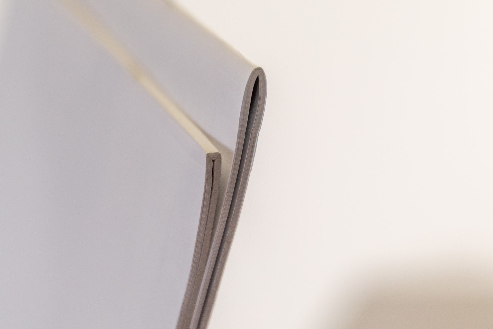 Close-up of a stack of gray paper with the top sheet slightly curled upwards, against a white background.