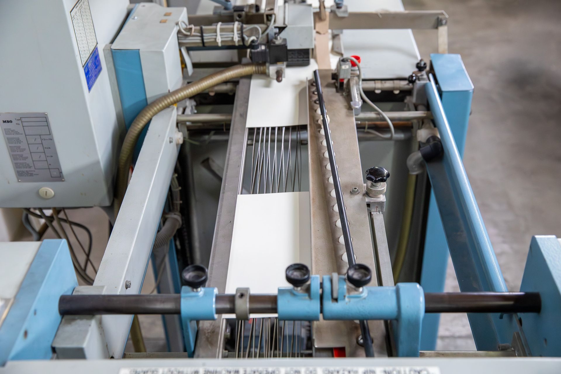 Industrial paper folding machine; white paper being fed through rollers and guides.