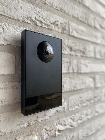 Op een bakstenen muur is een zwarte deurbel gemonteerd.