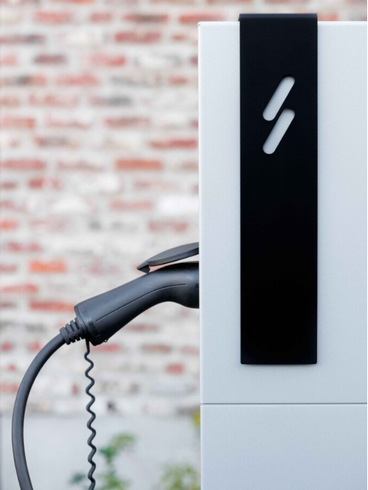 Een elektrische auto wordt opgeladen bij een laadstation voor een bakstenen muur.
