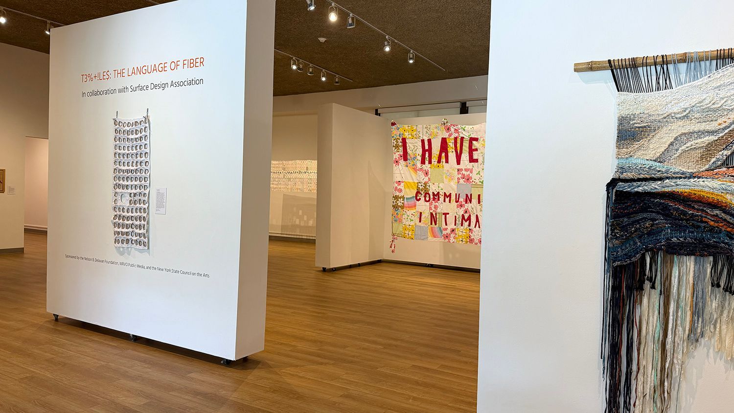 Art gallery with large hanging white panels displaying colorful abstract text and paintings on a wooden floor.