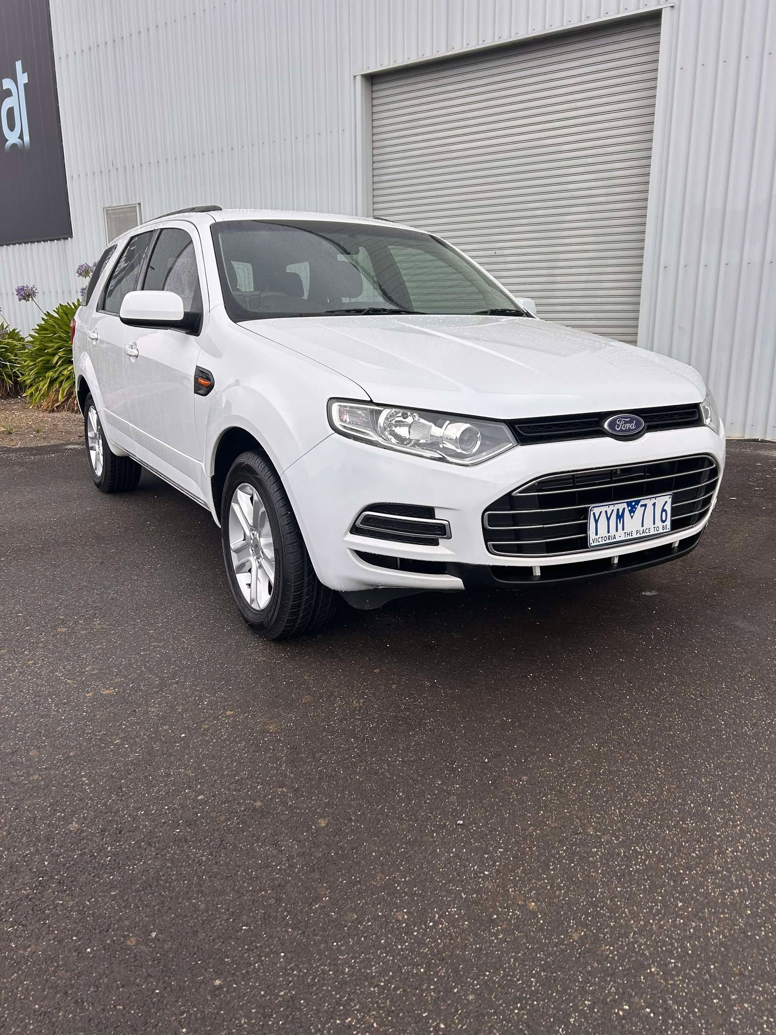 A white ford escape is parked in front of a building.